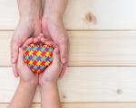 adult's hands holding child's hands with a multi-coloured jigsaw heart