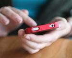 person holding a red mobile phone in their hand while tapping on the screen with the other hand