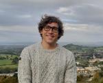 A photo of the children's author Tom Percival smiling with hills and countryside in the background