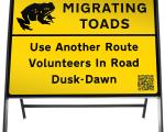 A photo of a road sign which reads migrating toads use another route volunteers in road dawn to dusk.