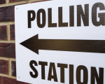 Sign on brick wall that reads 'Polling Station' with a directional arrow pointing left.