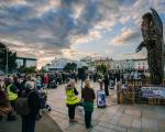 A crowd gathers around the Knife Angel, listening to a police officer speak