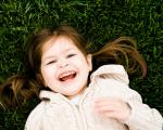 A girl dressed in a white hoodie lies on the grass and smiles at the camera 