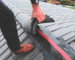 Close up of someone on a roof, holding up some of the roof tiles to show how badly the roofing work had been done.