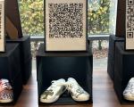 A pair of white trainers decorated with drawings in a black box, with a printed QR code displayed above.