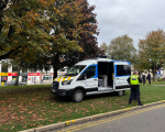 A van is parked on an area of grass with its back doors open, showing the workspace inside. Officials are in discussion nearby