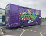 A purple bus decorated with artwork in a car park