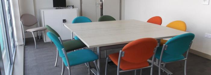 An interior of a meeting room with a red, blue, and yellow chairs around a table