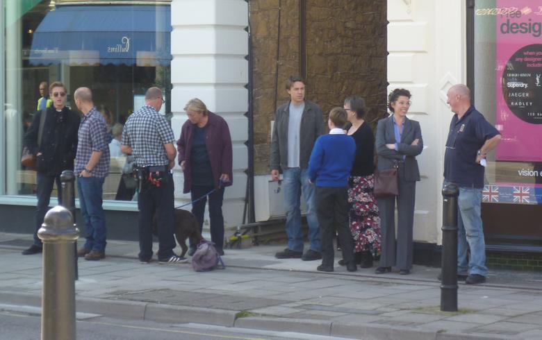 Actors and film crew stand in front of a shop window on Clevedon Hill Road waiting to film