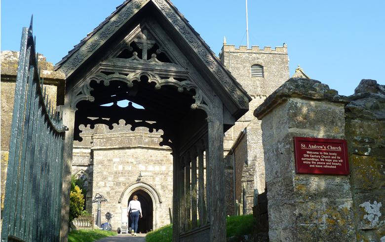 A carved wooden gate stands next to a stone pillar with a sign marking the entry to St Andrews Church