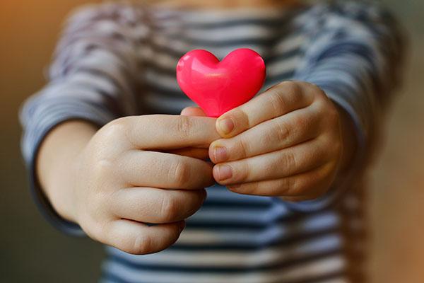 a child's hands holding a small pink heart towards the camera