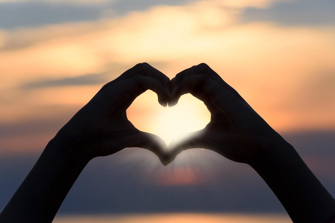 hands making a heart shape with a sunset in the background