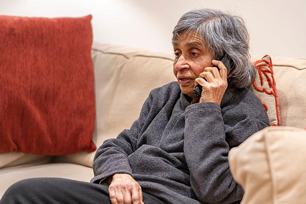 elderly lady wearing a grey sweatshirt and sitting on a sofa while talking on the phone