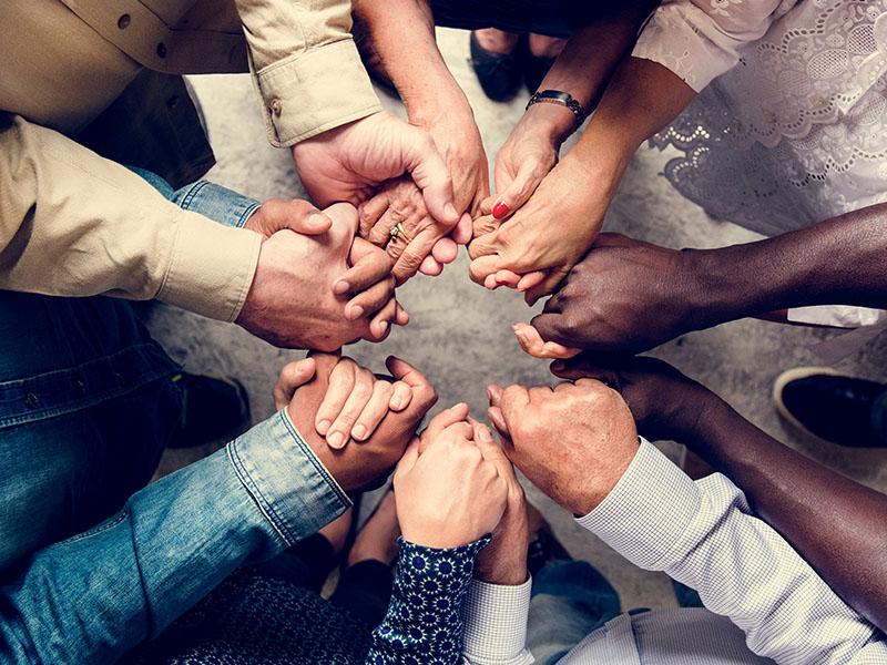 forearms of seven diverse people linking in the centre to form a circle