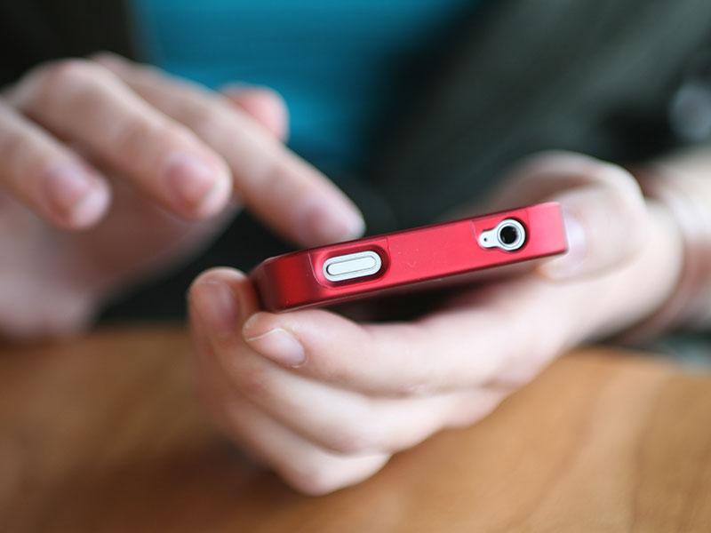 person holding a red mobile phone in their hand while tapping on the screen with the other hand