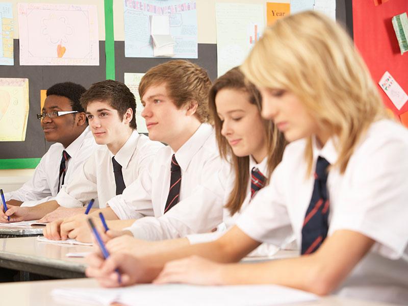 five teenagers wearing school uniform working at a desk