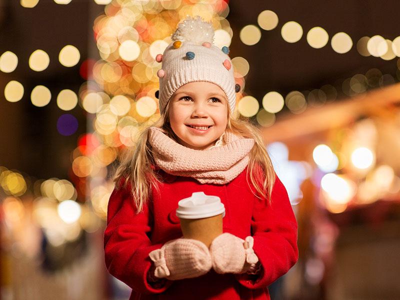 A girl in a red coat with Christmas lights in the background