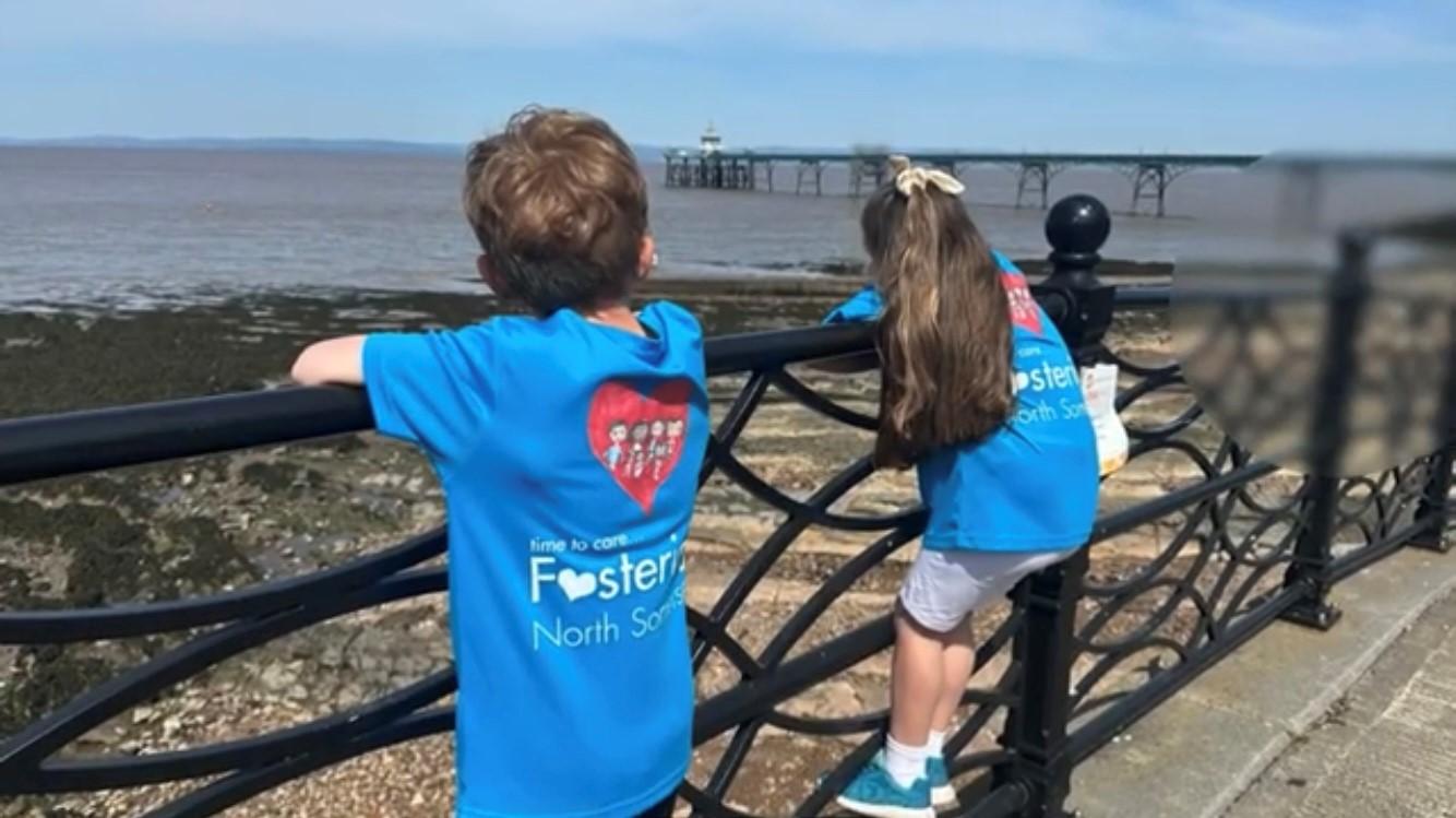 A boy and girl wearing North Somerset Fostering branded t-shirts standing by railings looking out towards Clevedon Pier