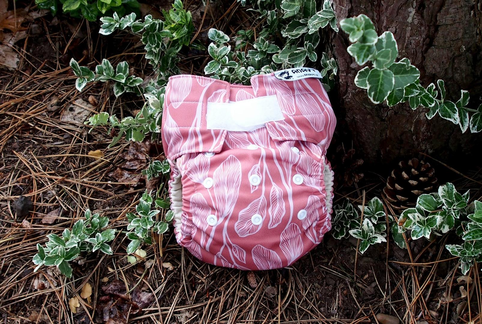 A pink patterned reusable nappy is positioned against a tree trunk, with leaves in the background