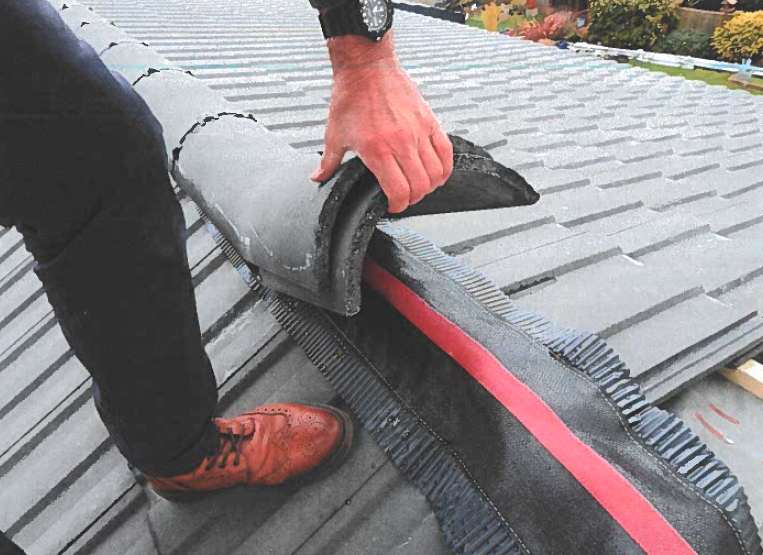 Close up of someone on a roof, holding up some of the roof tiles to show how badly the roofing work had been done.