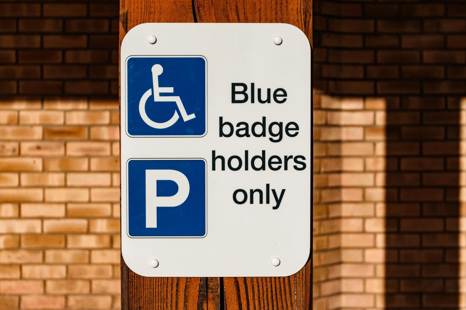 A white sign attached to a wooden post reads 'Blue badge holders only'