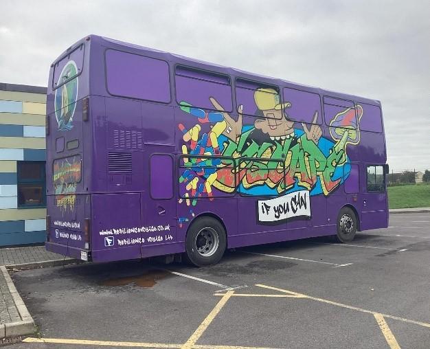 A purple bus decorated with artwork in a car park