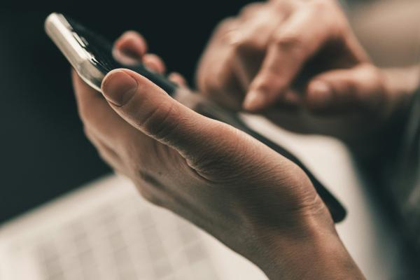 A photograph of a dark skinned person holding a phone in their hands and scrolling